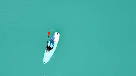 A girl in a dress floats on a glanders board on a pond with bright turquoise water. Warm summer day for travel. Top view from a quadcopter. Aerial photographyの写真素材