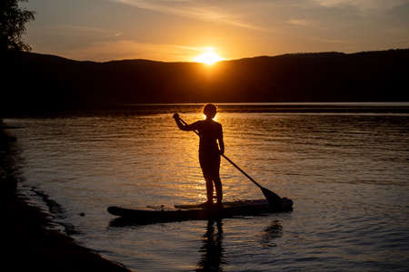 Girl on sup board with beautiful colored sunrise background mountains backgroundの写真素材