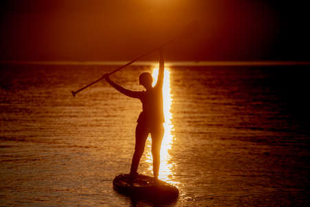 Girl on sup board with beautiful colored sunrise background mountains backgroundの写真素材