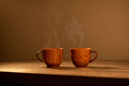Wooden mug with coffee. Steam comes from the cup from hot coffee, chocolate, tea. Christmas lights in the background. Christmas is coming soonの写真素材