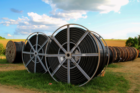 Black wire electric cable with wooden coil of electric cable under the skyの写真素材