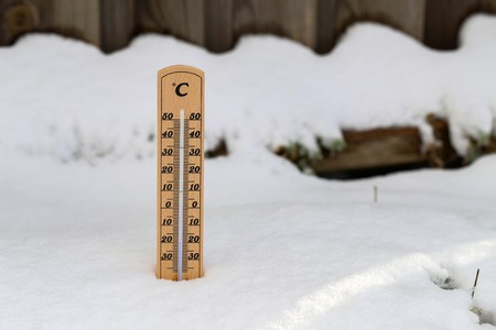 Wooden thermometer standing in snow, showing low temperature, space for text on the right. Winter...