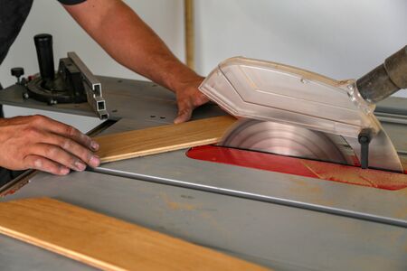 The worker cuts the parquet manually on a circular saw, and the sawdust flies off