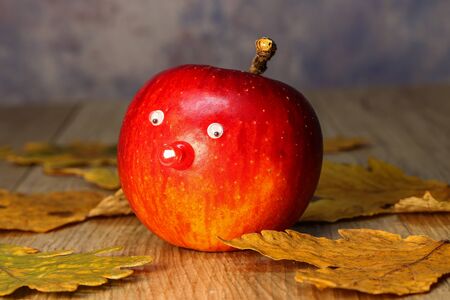 Beautiful red apple with eyes and nose is on the tableの写真素材