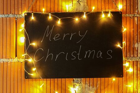 Merry Christmas - The inscription on the black chalkboard is illuminated by garlandsの写真素材