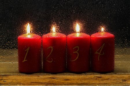 Advent candles in a row behind wet glass