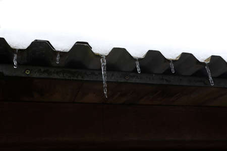 The snow on the roof melts and forms ice icicles.