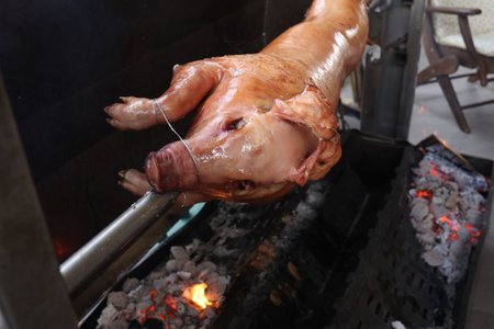 Pig is being grilled slowly on spit in traditional way, cooked with charcoal, fatty roasted meatの写真素材