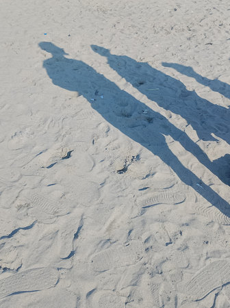 Shadows of tourists walking on sandy beach during sunny dayの写真素材