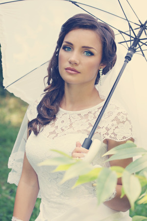 Beautiful bride in a hat with white umbrellaの写真素材