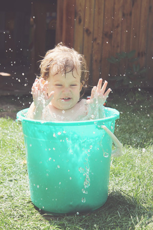Little girl bathes in a bucket in the yardの写真素材