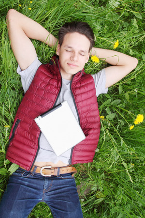 young man lying in the grass with iPadsの写真素材