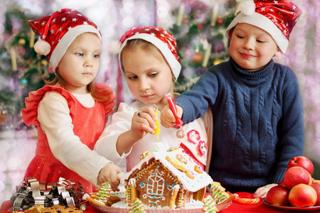 Three kids in caps decorated gingerbread houseの写真素材