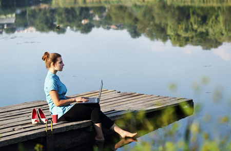 Concept illustrating remote work, business woman with laptop. She sits on the dockの写真素材