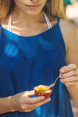A girl in blue dress eating passion fruitの写真素材