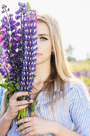 woman hiding behind a bouquet of lupinesの写真素材