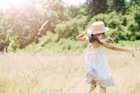 Little girl in a hat runs on a golden meadowの写真素材