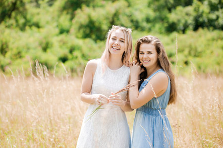 Two young beautiful cheerful girls walk in the fieldの写真素材