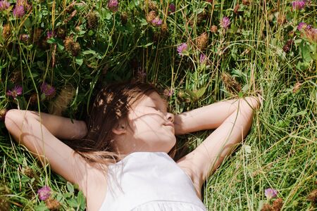 Beautiful girl in wildflowers resting on a sunny day in the meadowの写真素材