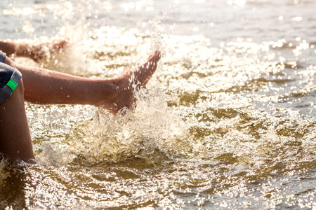 Boy makes splashing in a river sitting on a wooden pier