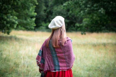 Young beautiful woman in a white beretin a cold autumn forest, view from the backの写真素材