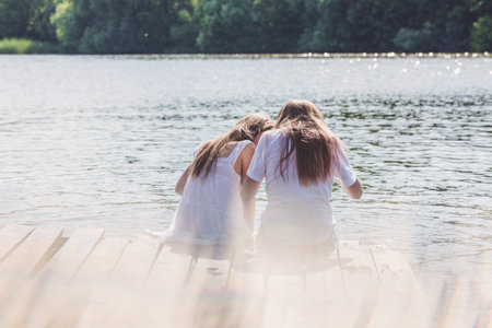 Two girls relax by the river in the rays of sunlight. Photos with highlightsの写真素材