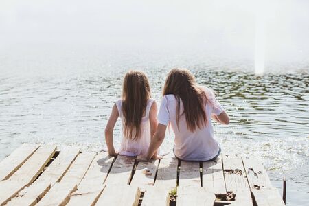 Two girls relax by the river in the rays of sunlight. Photos with highlightsの写真素材