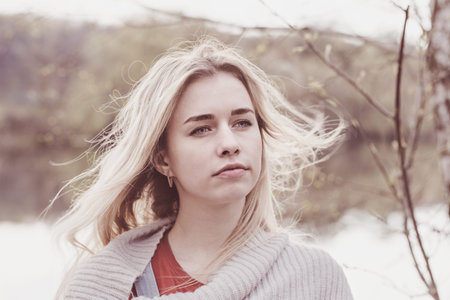 Portrait of a young beautiful sad blonde by the river with flowing hair