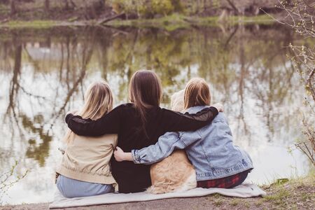 Three girls relaxing by the river with a dogの写真素材