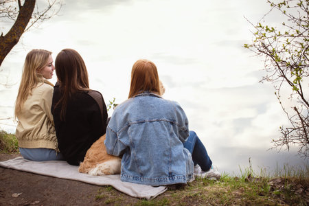 Three girls relaxing by the river with a dogの写真素材