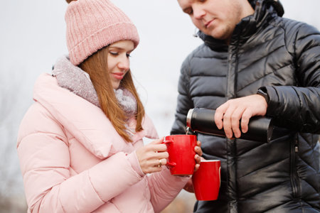 Young beautiful couple at a picnic in winter they drink coffee