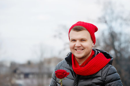 Handsome young man with red rose in hands outdoors in snowy weather. The concept for St. Valentine's...