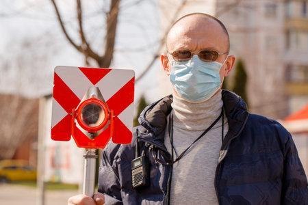 Surveyor holds a geodetic reflector in a protective mask. Coronavirus Protection Concept