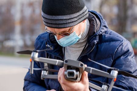 Surveyor in a protective mask prepares a quadcopter for photogrammetry. Coronavirus Protection Conceptの写真素材