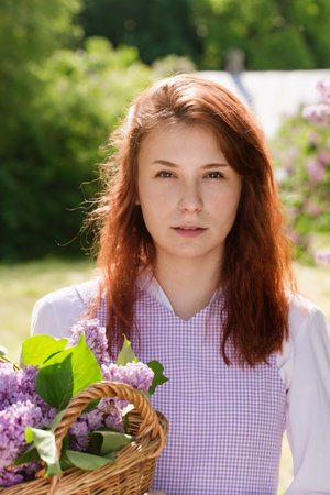 Young beautiful red-haired woman in a vintage dress in a garden with blooming lilacの写真素材