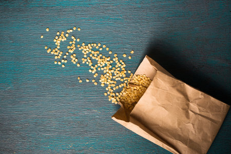 Paper bag with dry pepper seeds on wooden background