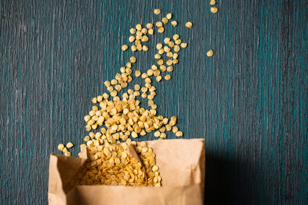 Paper bag with dry pepper seeds on wooden background