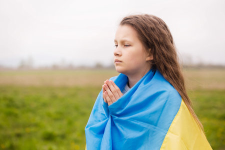 A little girl with the flag of Ukraine prays for the victory of her countryの写真素材