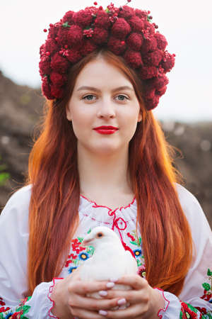 A beautiful Ukrainian woman in Ukrainian national embroidered dress with a white dove in her hands, a symbol of peace in Ukraineの写真素材