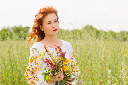 A woman in a Ukrainian folk costume in a field with a bouquet of wild flowersの写真素材