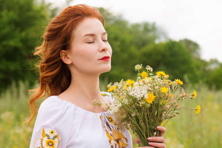 A woman in a Ukrainian folk costume in a field with a bouquet of wild flowersの写真素材