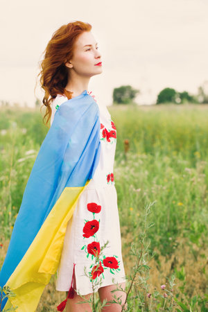 A beautiful Ukrainian woman in a folk dress with a flag of Ukraine is walking along the fieldの写真素材