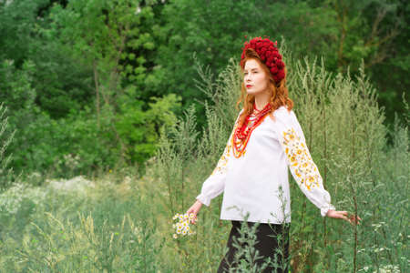 A beautiful red-haired Ukrainian woman in a folk dress with a bouquet of daisiesの写真素材