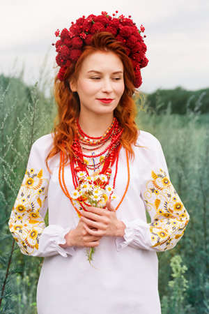 A beautiful red-haired Ukrainian woman in a folk dress with a bouquet of daisiesの写真素材