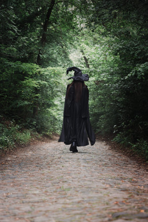 A witch in a black cloak and a big black hat in a dark forest. Halloween concept