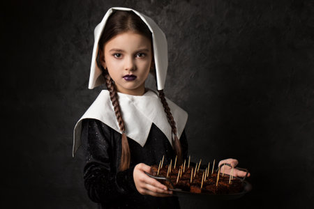 Gothic girl with pigtails in a cap holds a tray with chocolate cake on a dark backgroundの写真素材