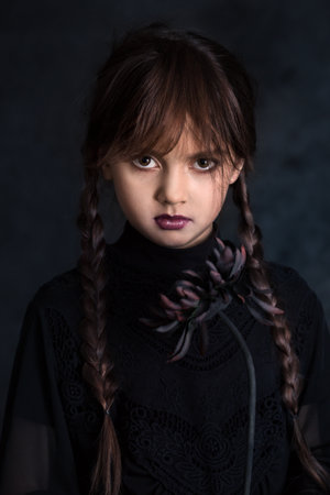A sullen little girl with pigtails is holding a black dahlia flower. Gothic style on a dark backgroundの写真素材