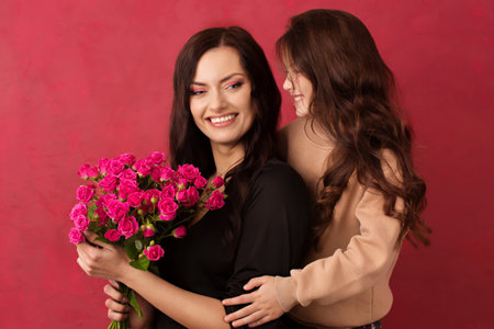 The girl greets her mother with a beautiful bouquet of pink roses on a pink background. Color of background Viva Magenta 18-1750, in 2023の写真素材