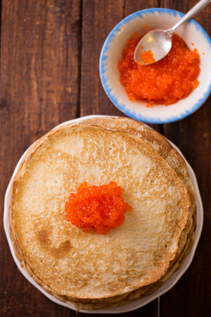 Delicious thin ruddy pancakes in a plate with red caviar on a wooden backgroundの写真素材