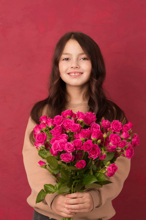 A teenage girl with a bouquet of beautiful pink roses on a pink background.の写真素材